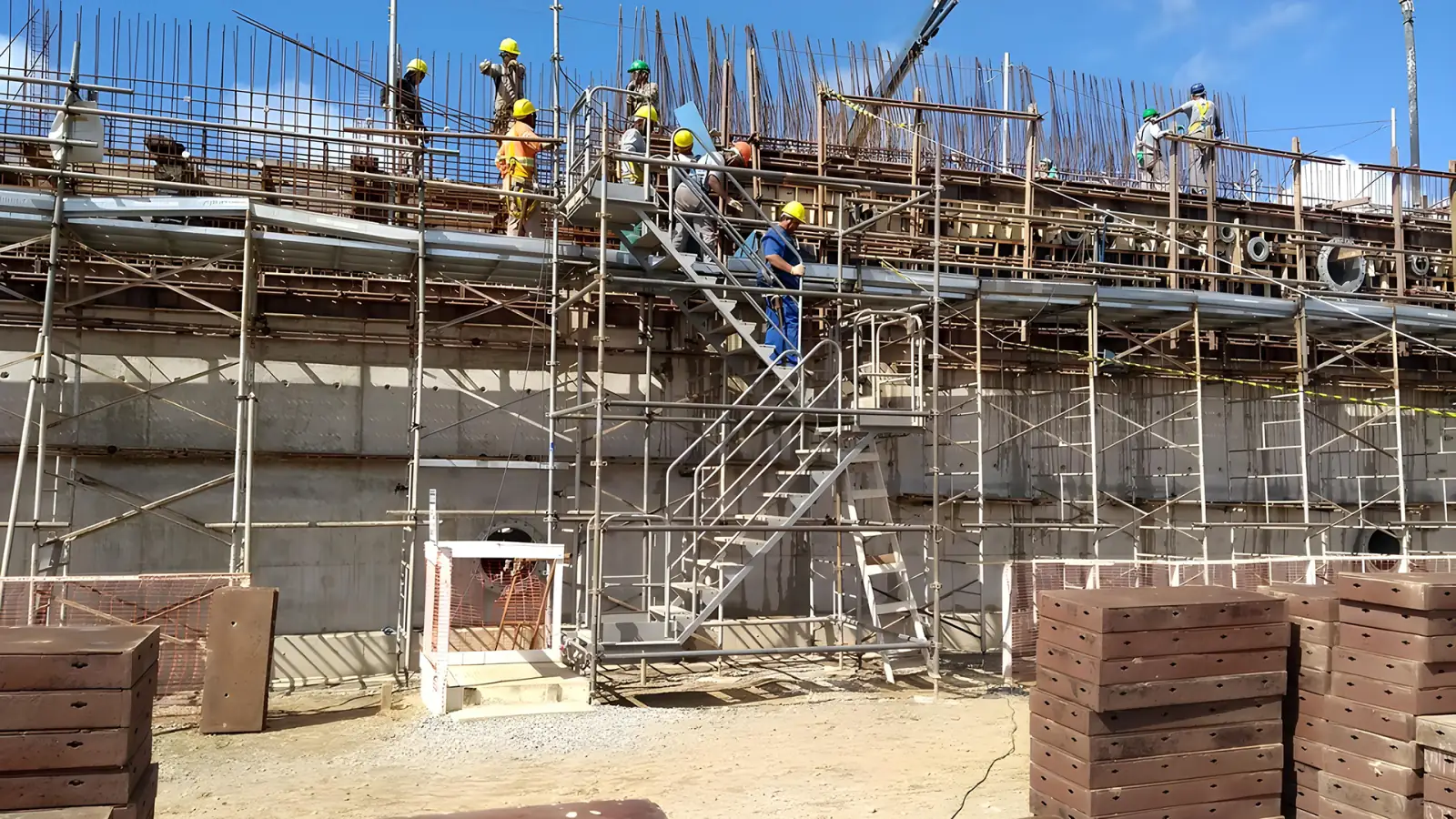 Obra com formas de parede e equipe no topo, controle de tolerância dimensional em estrutura de concreto
